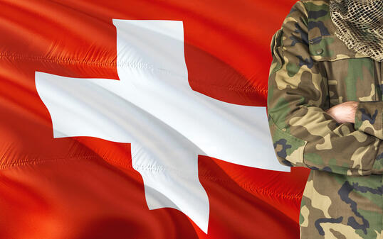 Crossed arms Swiss soldier with national waving flag on background - Switzerland Military theme.