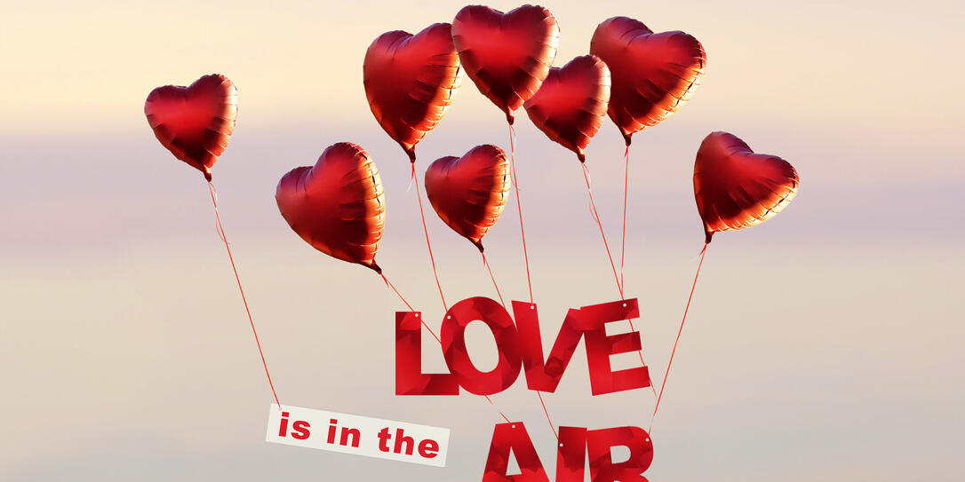 sunset sky with red heart shaped air balloons with text love is in the air at the sky