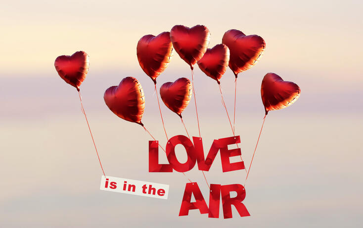 sunset sky with red heart shaped air balloons with text love is in the air at the sky