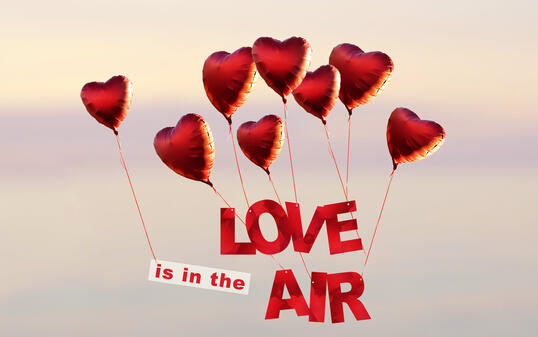 sunset sky with red heart shaped air balloons with text love is in the air at the sky