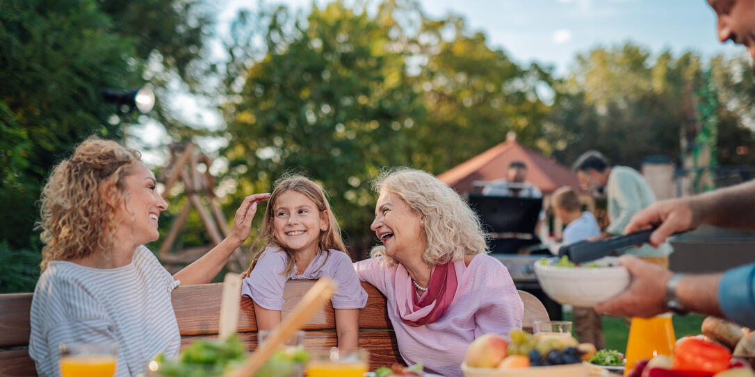 Happy family enjoying backyard barbecue: grandmother, mother, and daughter sharing a laugh