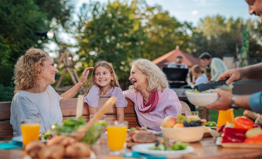Happy family enjoying backyard barbecue: grandmother, mother, and daughter sharing a laugh