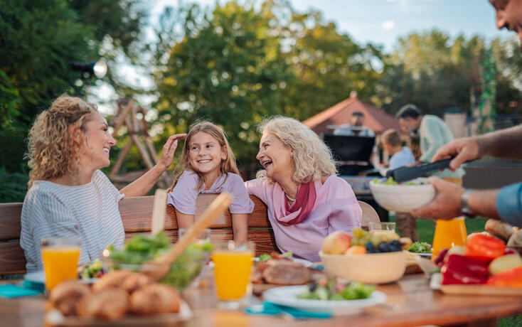 Happy family enjoying backyard barbecue: grandmother, mother, and daughter sharing a laugh