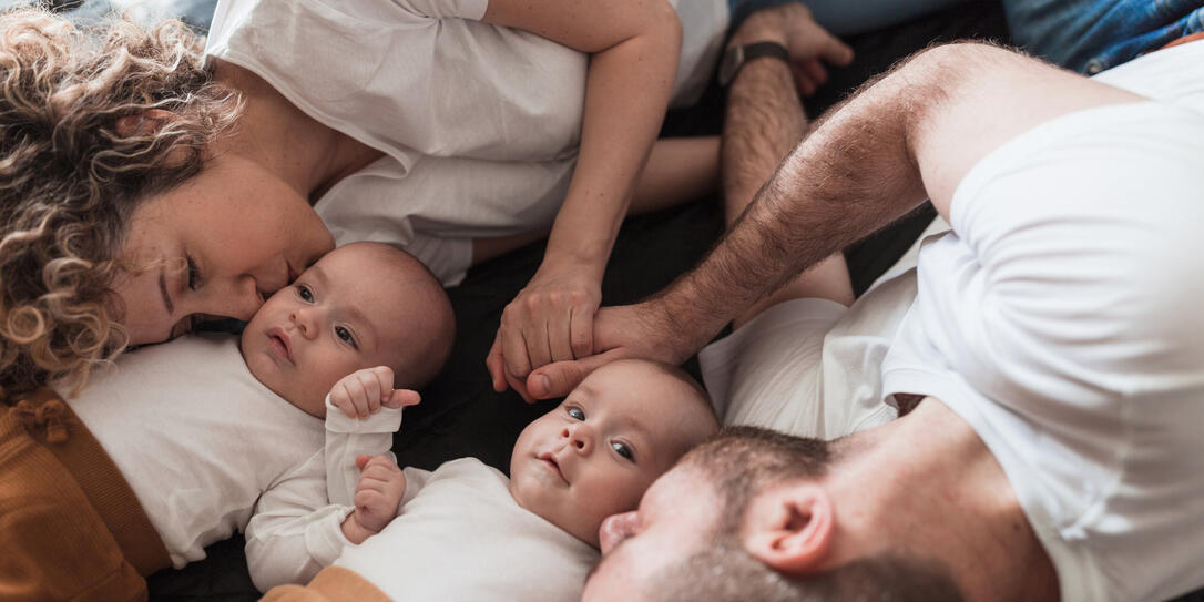 Parents holding hands and resting by their twin babies and kissing them