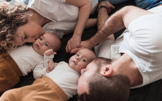 Parents holding hands and resting by their twin babies and kissing them