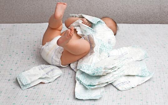 A baby in a diaper lies on a white background plays with a stack of diapers. Copy space for text