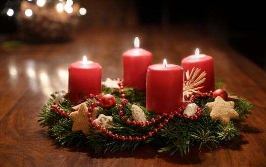 Fourth Advent - decorated Advent wreath from fir branches with red burning candles on a wooden table in the time before Christmas, festive bokeh in the warm dark background, copy space, selected focus