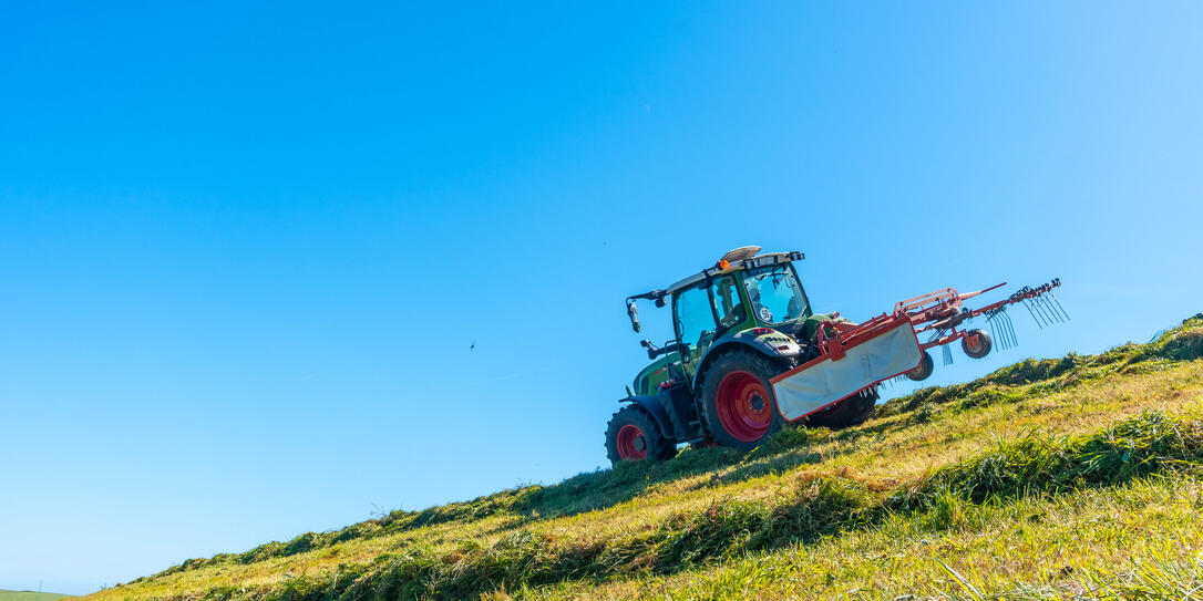 A tractor is driving down a hill, plowing the grass