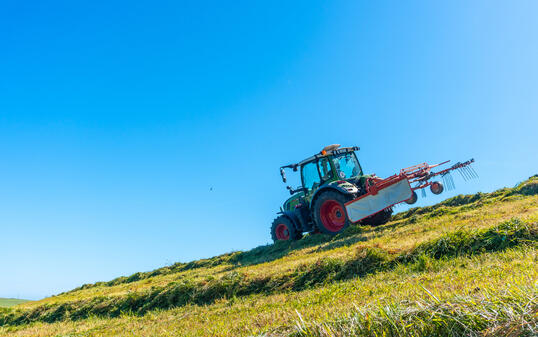 A tractor is driving down a hill, plowing the grass