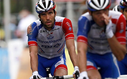 Thibault Pinot (links) mit dem zerfetzten Shirt überquert nach dem Sturz zu Beginn der Tour der France frustriert die Ziellinie.