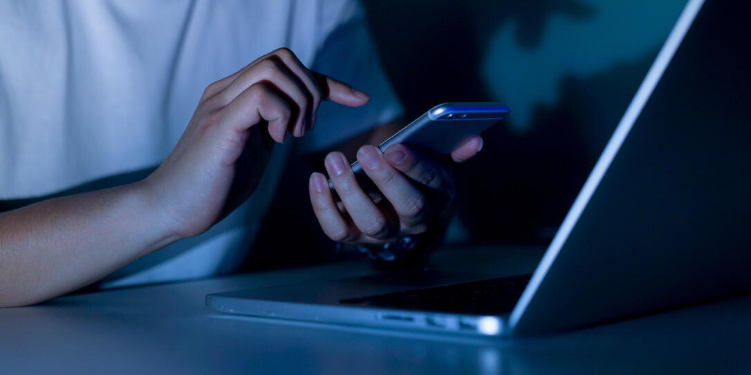 close up young man hand holding smartphone for access by unlock on screen and using laptop for register website on internet in the late night , internet addiction concept