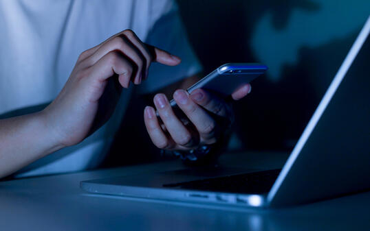 close up young man hand holding smartphone for access by unlock on screen and using laptop for register website on internet in the late night , internet addiction concept
