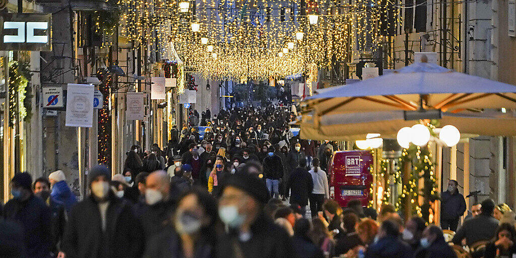 Zahlreiche Menschen mit Mund-Nasen-Schutz gehen eine weihnachtlich geschmückte Einkaufsstraße in der Innenstadt entlang. Foto: Andrew Medichini/AP/dpa