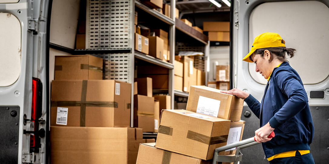 Smiling courier loading hand truck, stacking packages