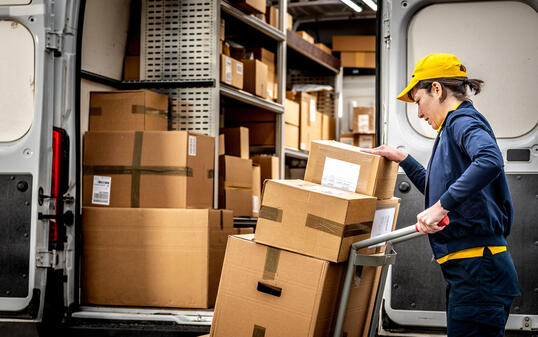 Smiling courier loading hand truck, stacking packages