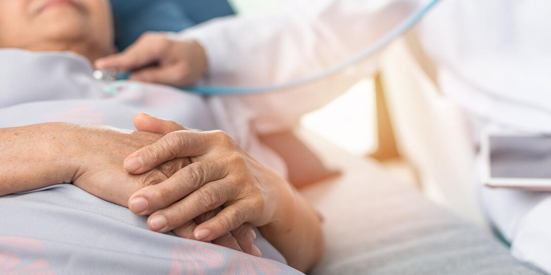 Hospitalized elderly patient, senior old aging woman laying on bed with cardiologist doctor or physician examining cardiological heart health, checking pulse in hospital clinic exam room